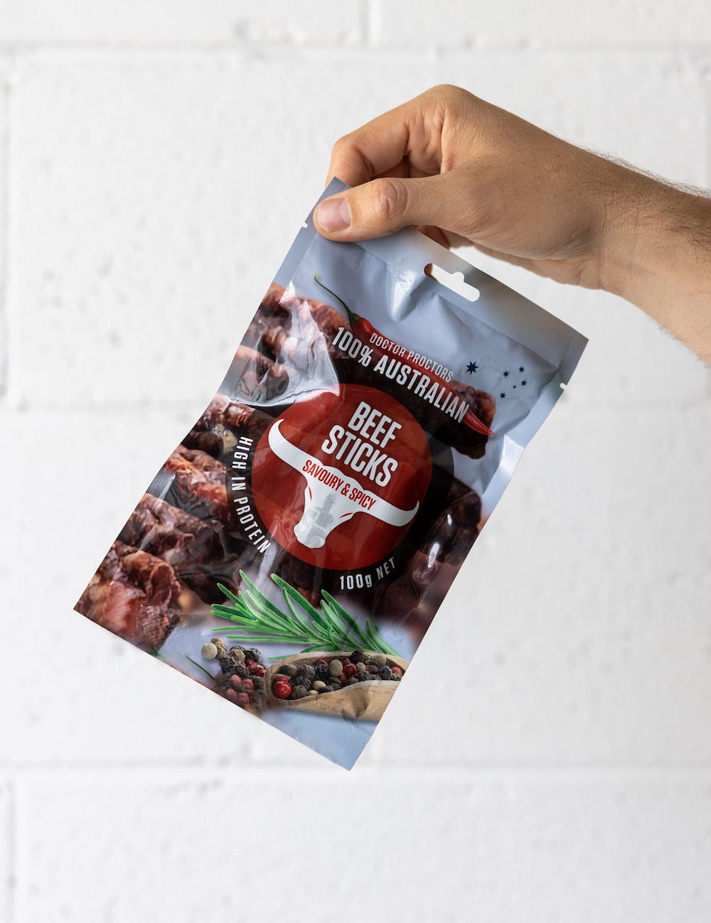 Hand holding a pouch of beef sticks up in the air in front of a white brick wall
