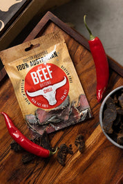 Small packet of chilli beef biltong next to fresh chillis and a bowl of biltong
