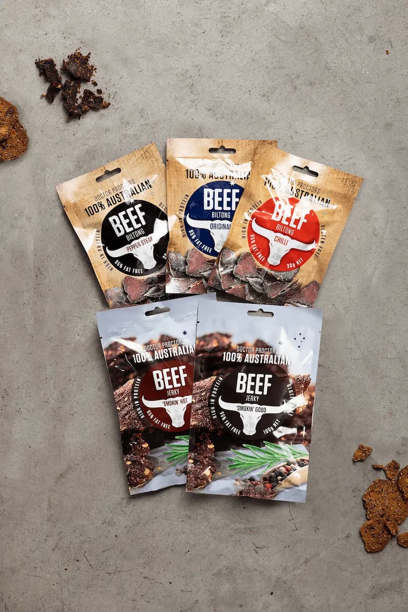 5 pouches of biltong spread out on table next to biscuits and loose pieces of biltong