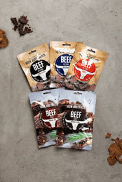 5 pouches of biltong spread out on table next to biscuits and loose pieces of biltong