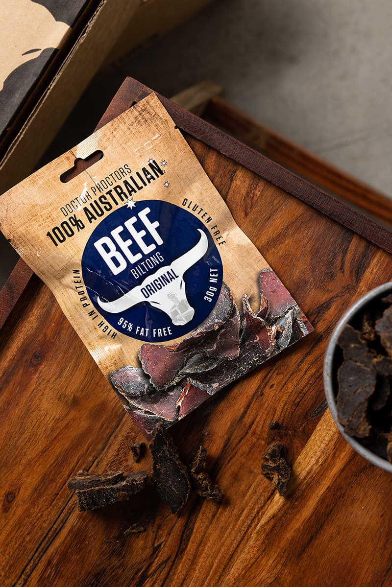 Small pouch of original biltong sitting on wooden table next to a bowl of biltong