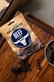 Small pouch of original biltong sitting on wooden table next to a bowl of biltong