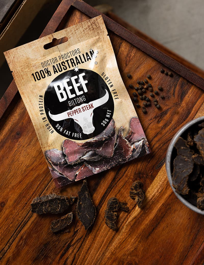 Small pouch of biltong on table next to pepper corns and large pieces of pepper steak biltong