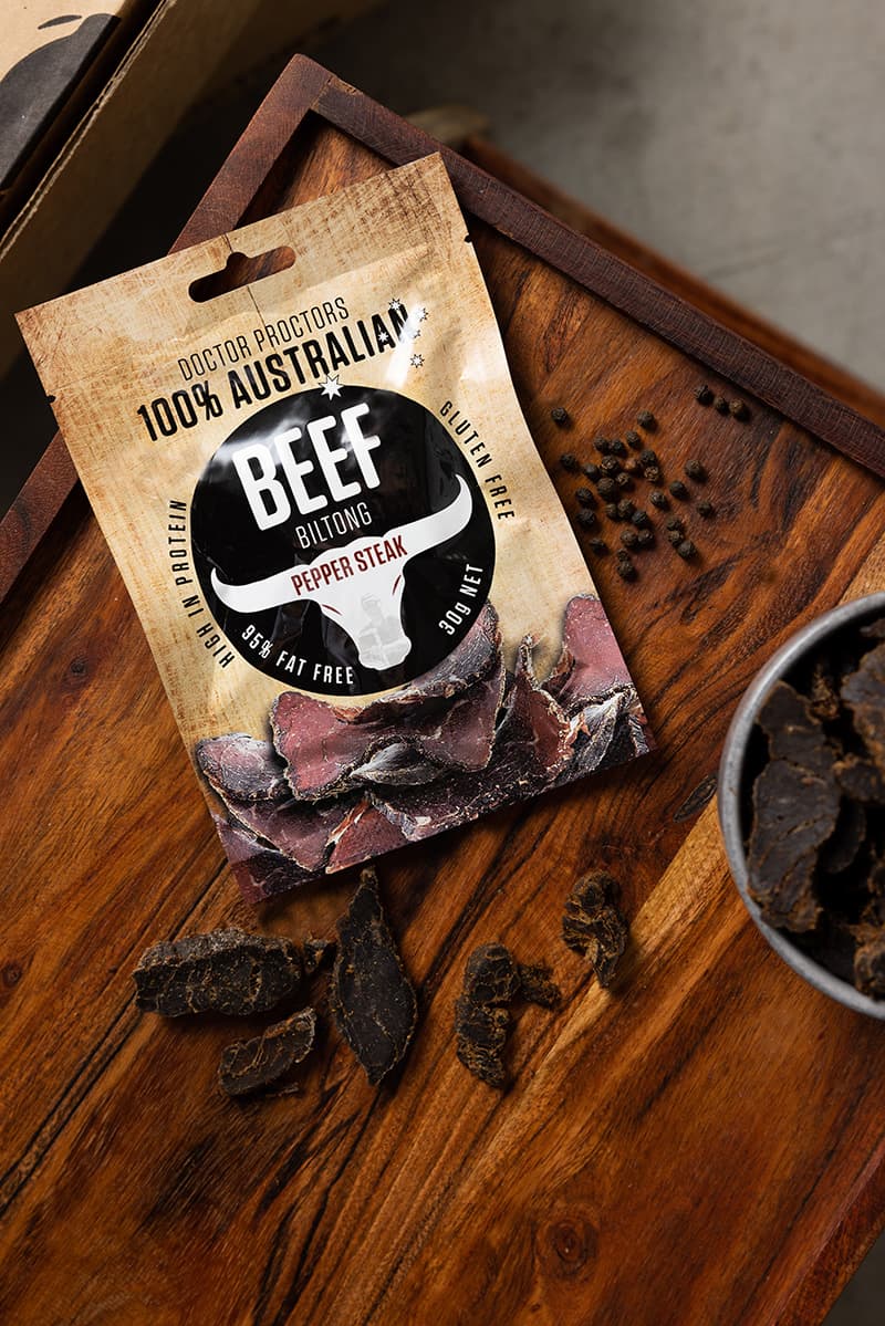 Small pouch of biltong on table next to pepper corns and large pieces of pepper steak biltong
