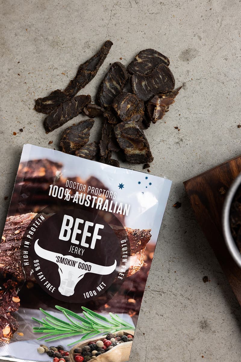 Pouch of smoked beef jerky on table next to fatty and tended pieces of jerky