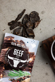Pouch of smoked beef jerky on table next to fatty and tended pieces of jerky