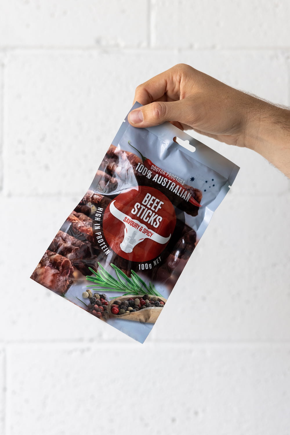 Hand holding a pouch of beef sticks up in the air in front of a white brick wall