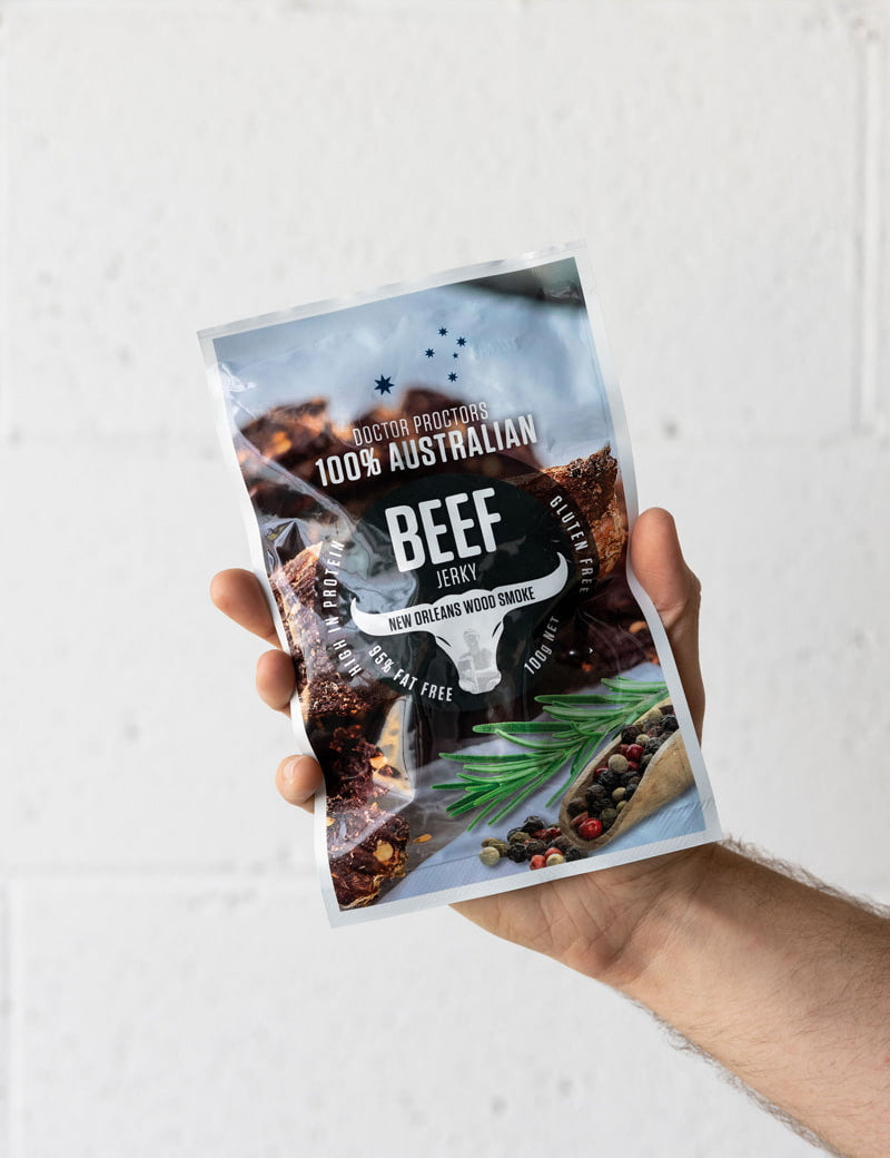 Hand holding large pack of wood smoked beef jerky up in the air in front of a white brick wall