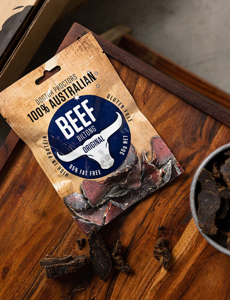 Small pouch of original biltong sitting on wooden table next to a bowl of biltong